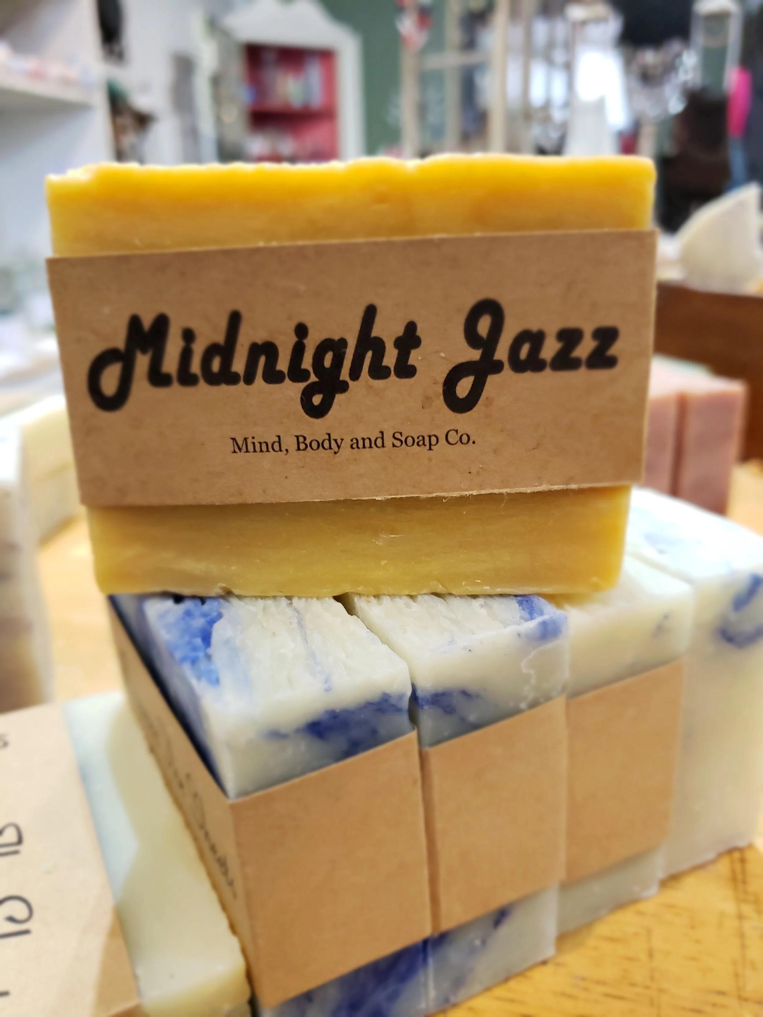A photo of a rectangular block of soap with a tan label wrapped around it. The soap is a creamy color with a smooth surface and has a simple design.