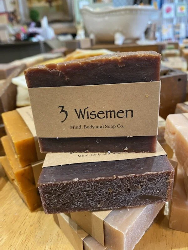 A photo of a rectangular block of soap with a tan label wrapped around it. The soap is a creamy color with a smooth surface and has a simple design.