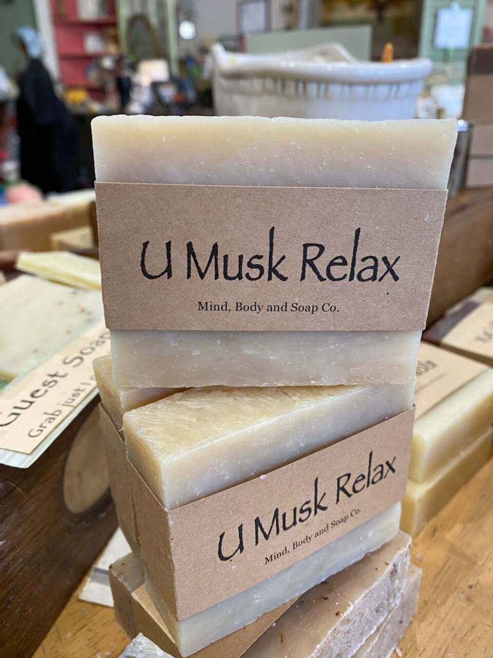 A photo of a rectangular block of soap with a tan label wrapped around it. The soap is a creamy color with a smooth surface and has a simple design.