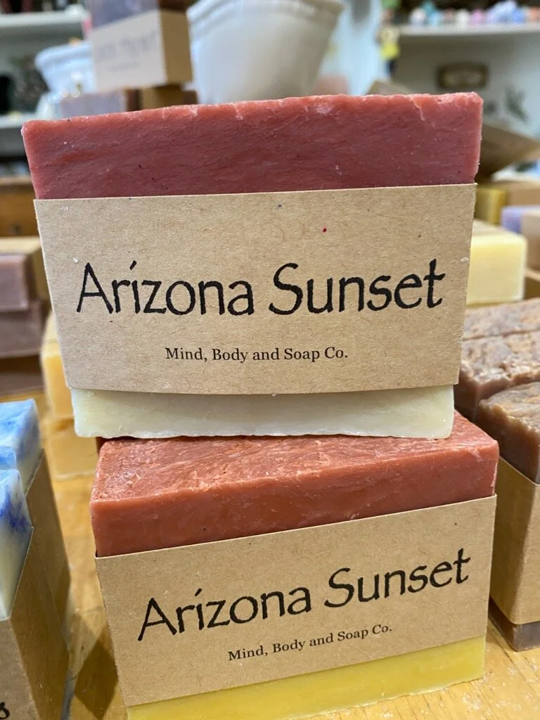 A photo of a rectangular block of soap with a tan label wrapped around it. The soap is a creamy color with a smooth surface and has a simple design.