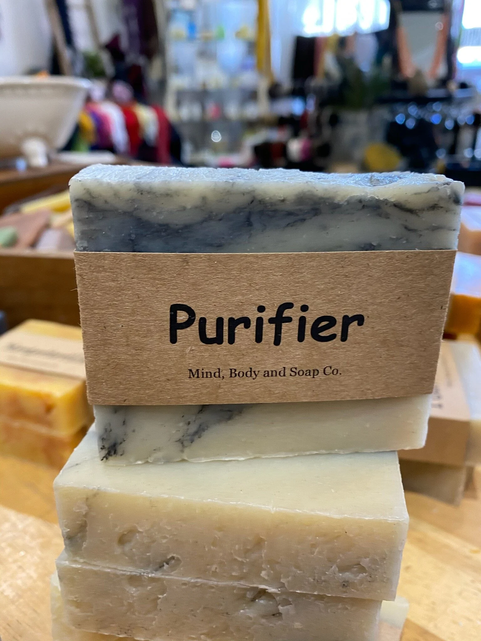 A photo of a rectangular block of soap with a tan label wrapped around it. The soap is a creamy color with a smooth surface and has a simple design.