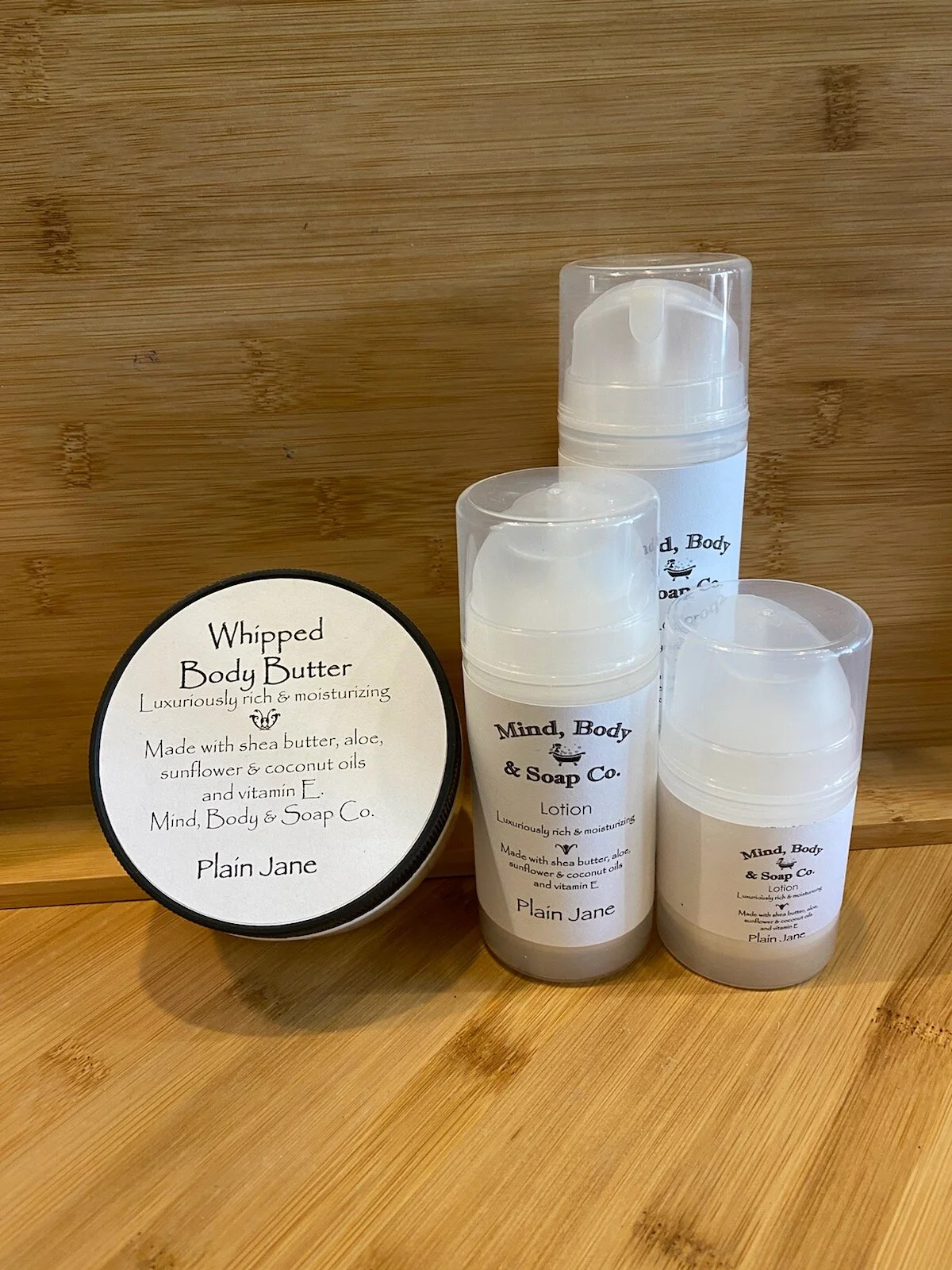 Three sizes of lotion bottles and a round tube of body butter. The lotion bottles are clear and the inside is a creamy texture.