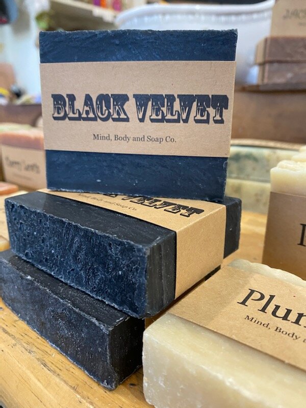 A photo of a rectangular block of soap with a tan label wrapped around it. The soap is a creamy color with a smooth surface and has a simple design.