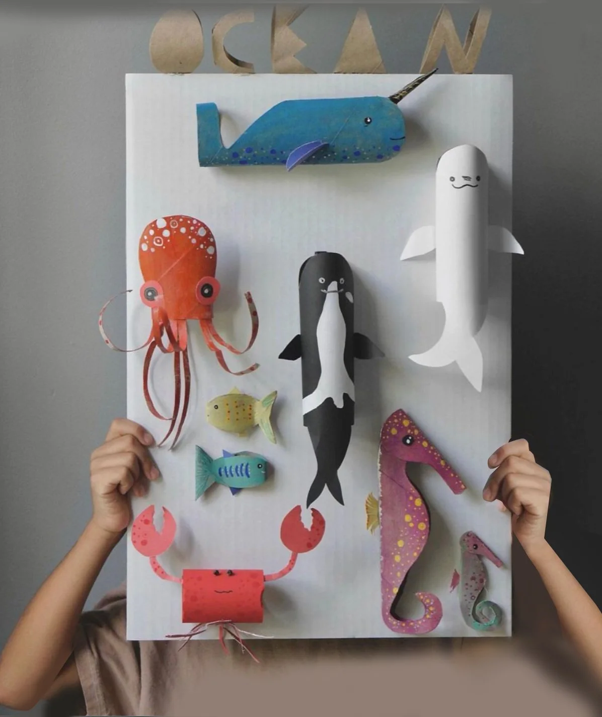 Colorful paper cutout sea life with a whale, octopus, fish, crab, and seahorse on a white poster board.