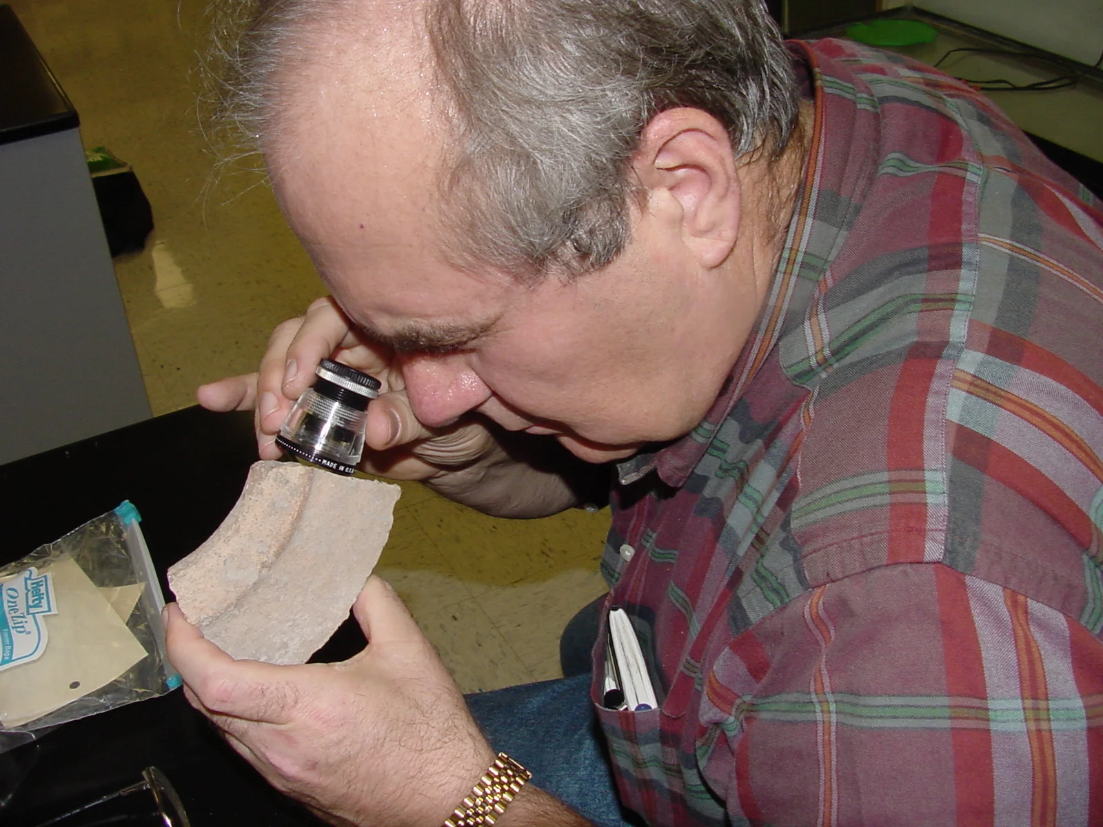   Once the sherd is cut, the color and texture of the fabric used to construct the vessel is clearly revealed. The archaeologist carefully views the fabric with a magnifying instrument called a "comparator." On the lens of the comparator are a series