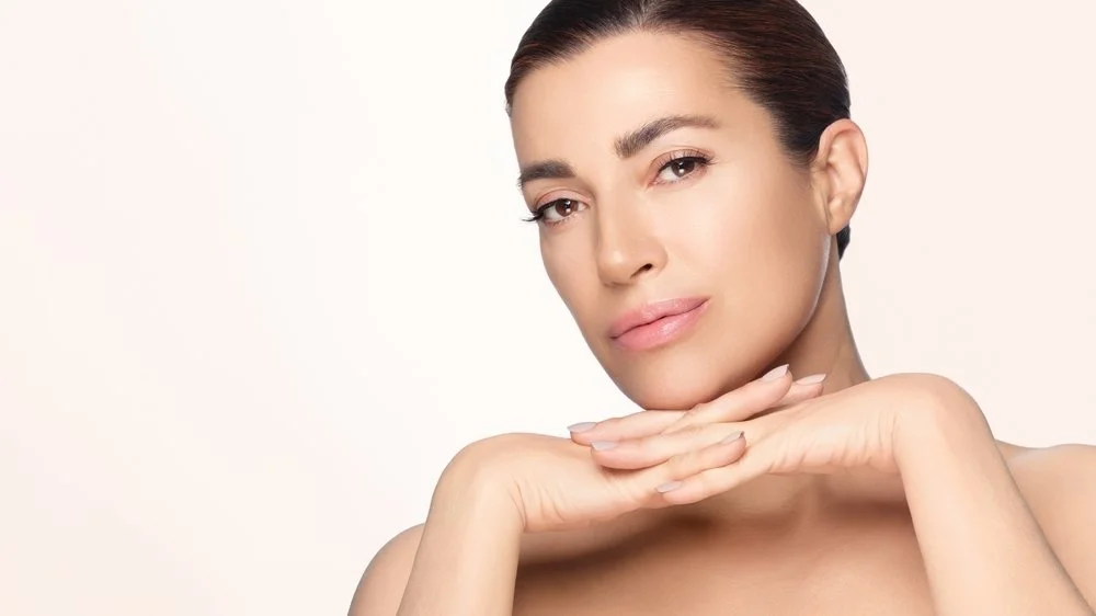 Woman with long hair posing with a palm leaf against a neutral background.