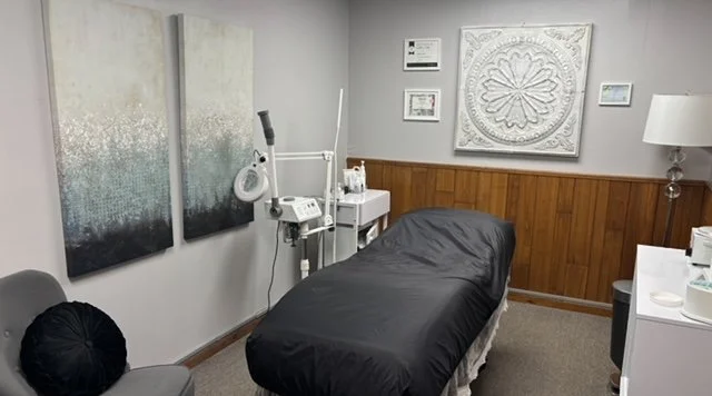 Medical examination room with a treatment bed covered in black sheet, medical equipment, wall art, and a lamp.