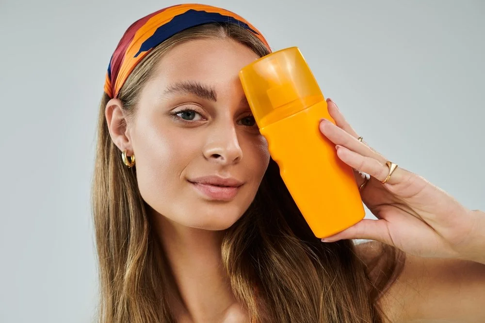 A woman with a bandana in her hair holding a yellow bottle of product against her forehead