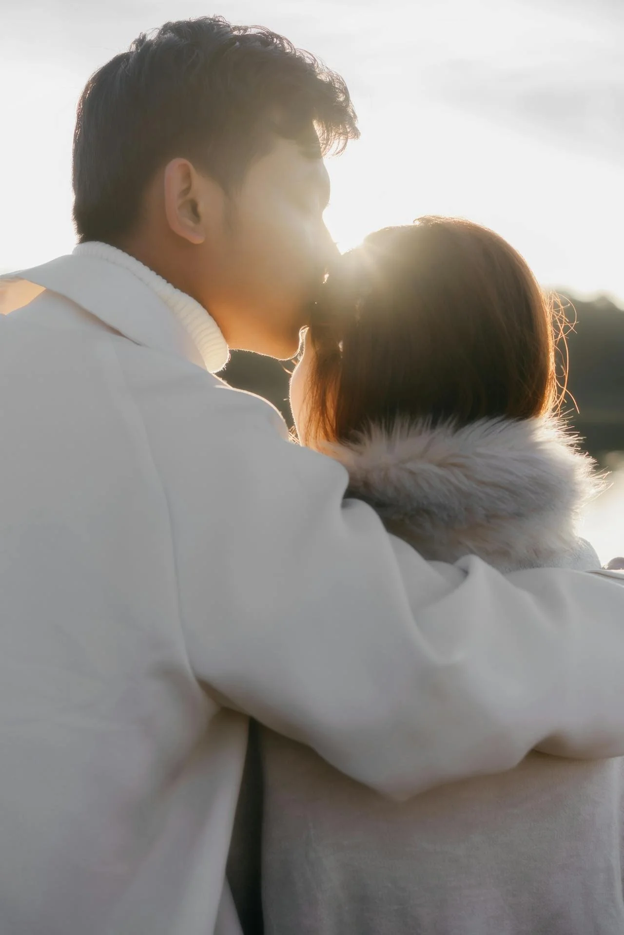 A couple sharing a kiss outdoors with the sun setting behind them.