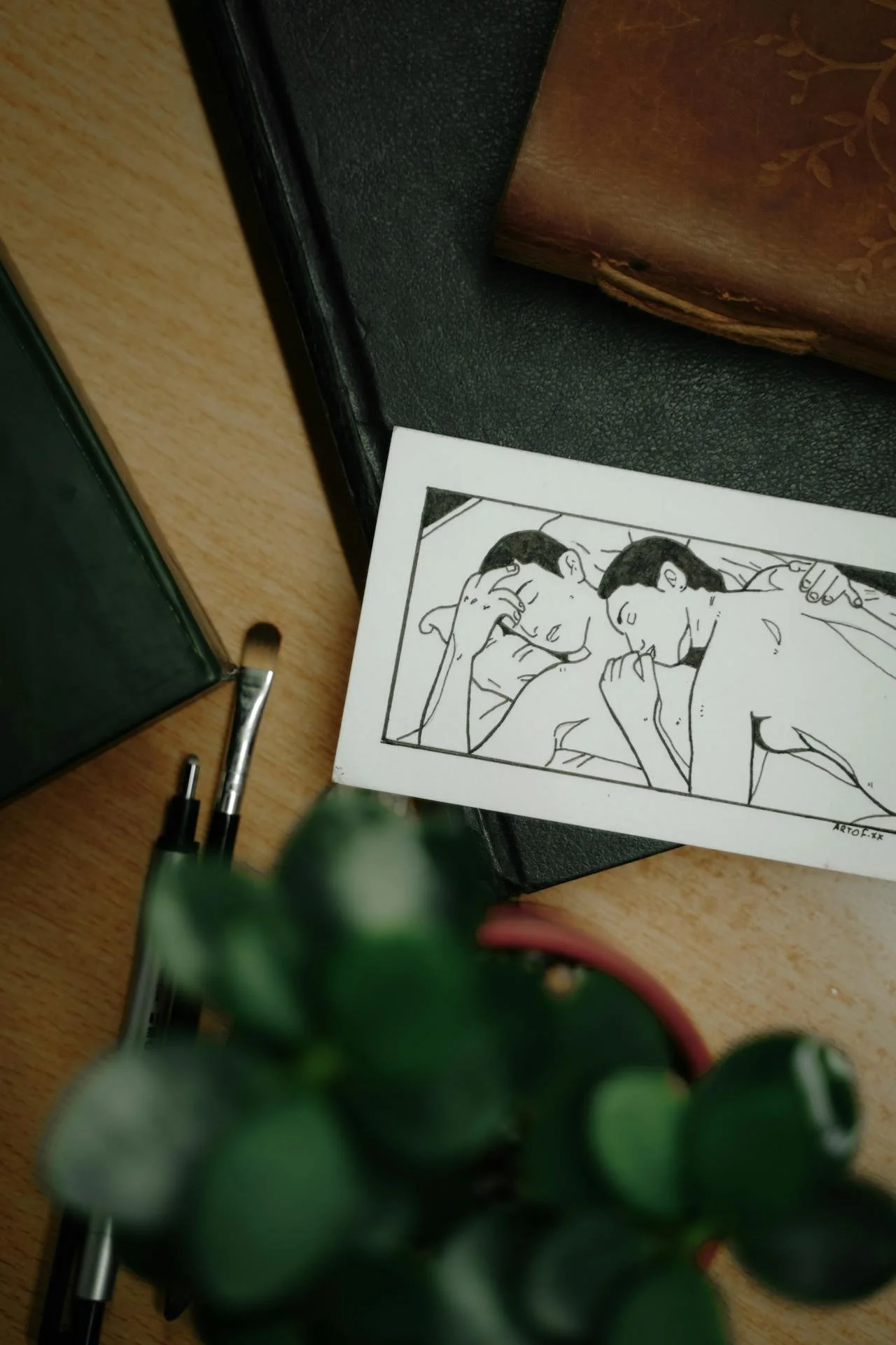 A black and white illustration of two men lying on a bed, facing each other, with one touching his forehead and the other resting his arm near his head, on a piece of paper.