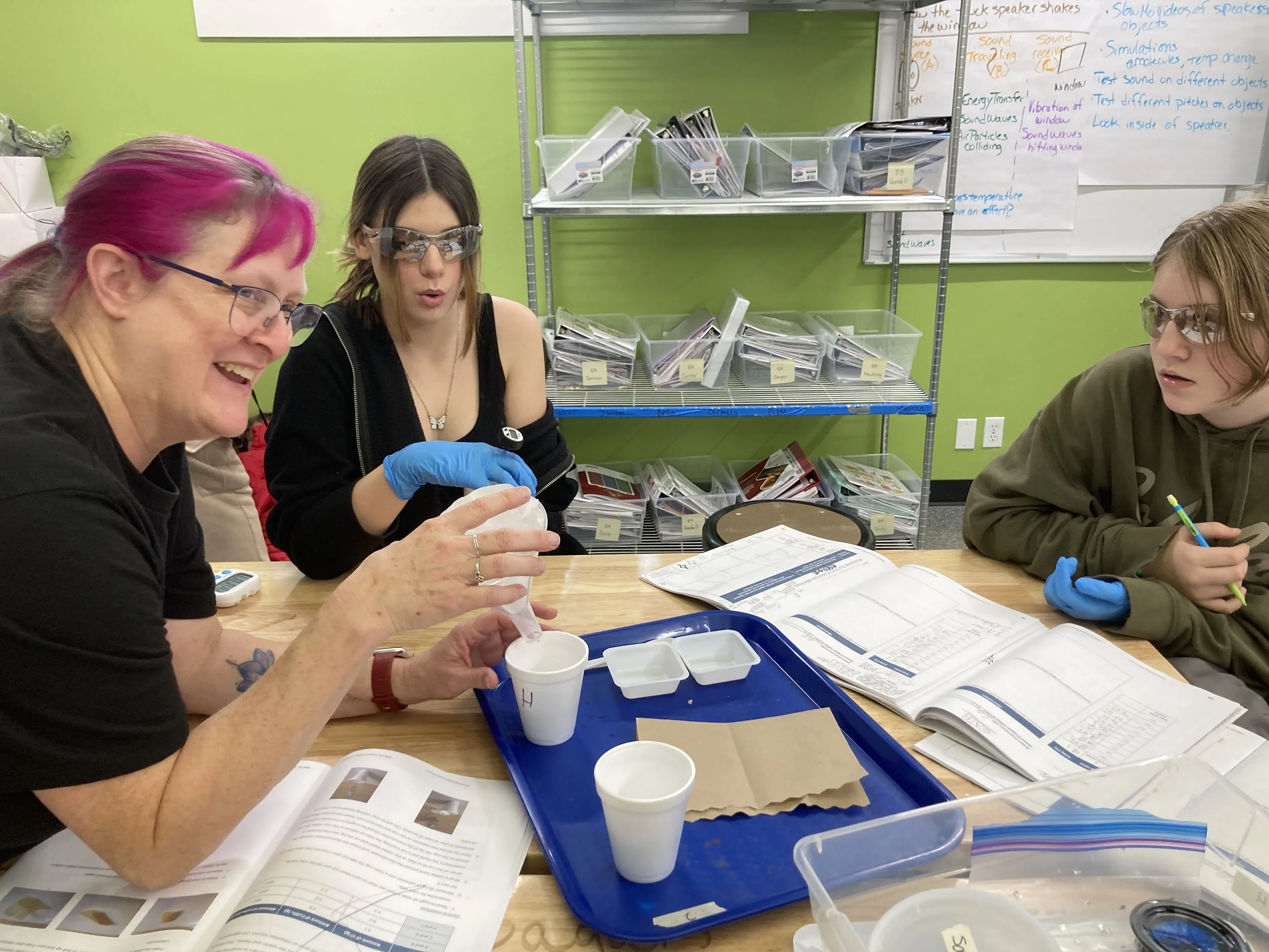 Mountain landscape with snow-capped peaks in the background, rolling grassy hills in the foreground, and a modern wooden building nestled on the hillside.