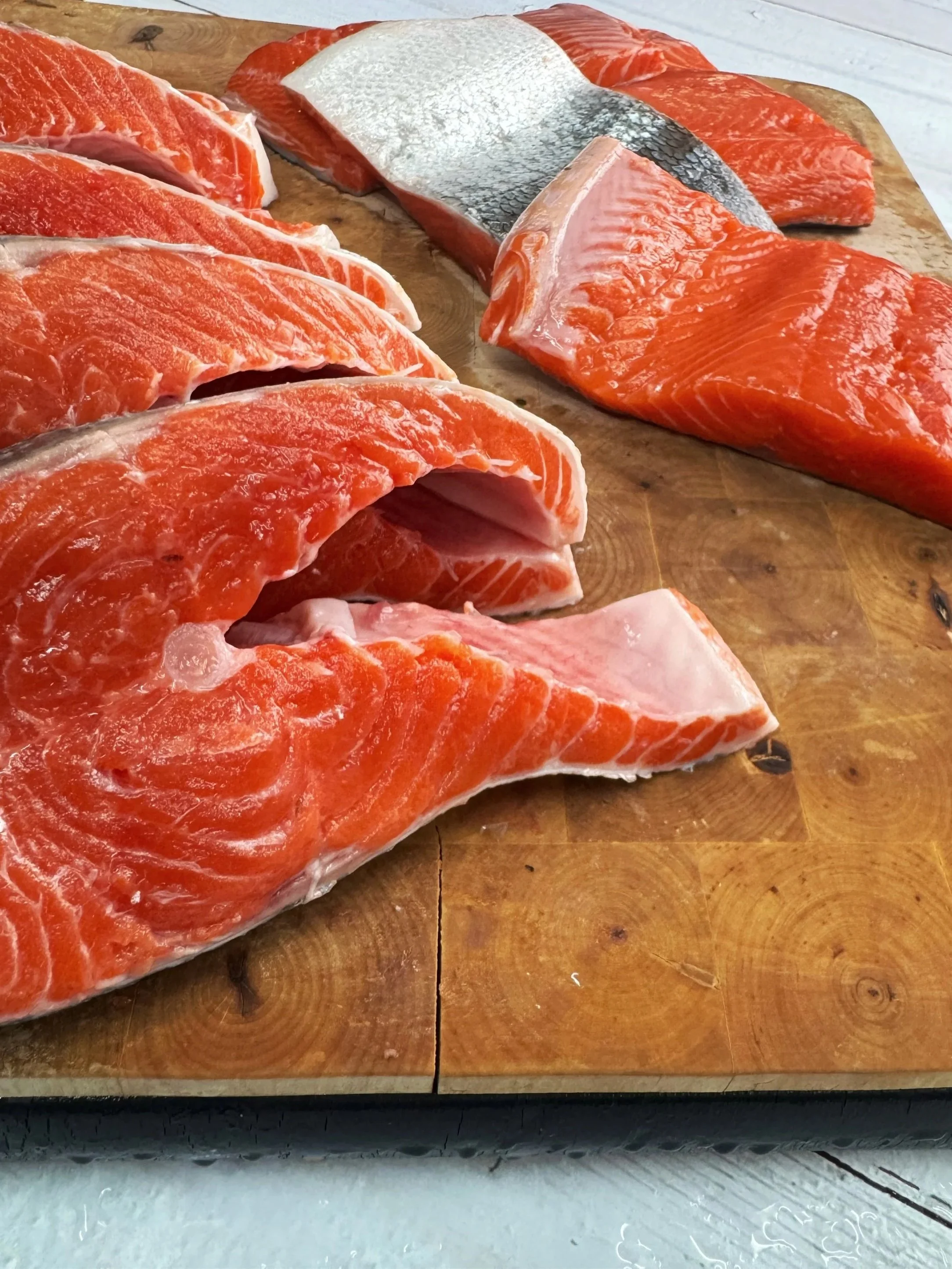 Fresh sockeye salmon fillets and portions displayed on a wooden cutting board at Ocean Odyssey Inland, Edmonton's local seafood shop