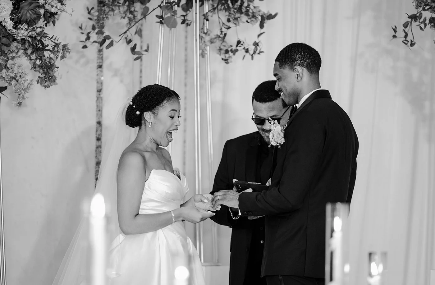 Bride smiling as her groom puts a wedding band on her finger