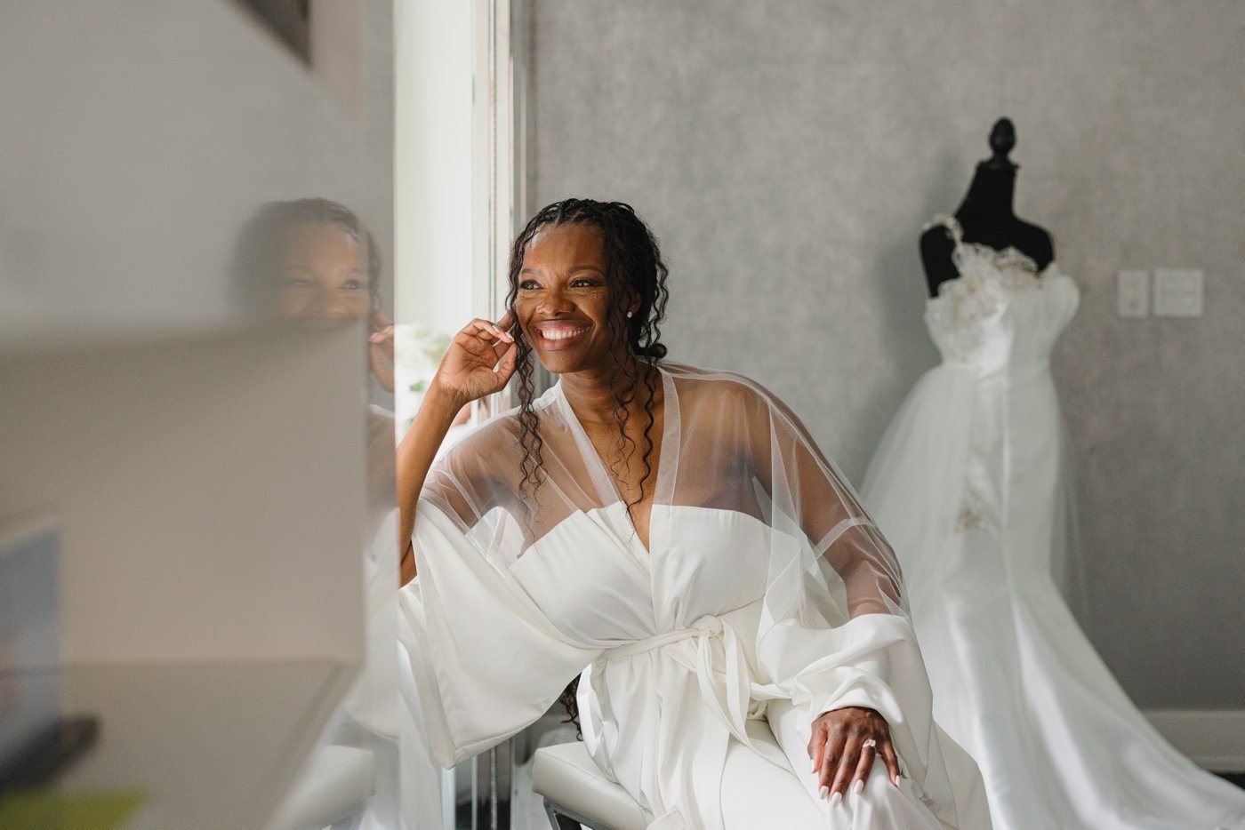 Bride in a white robe looking out the window of her hotel room