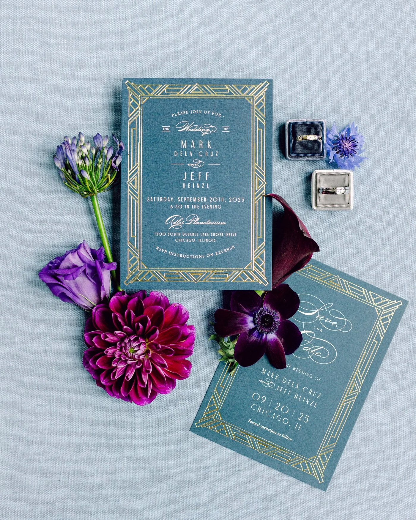 Flatlay of a blue and gold Art Deco wedding invitation with purple flowers