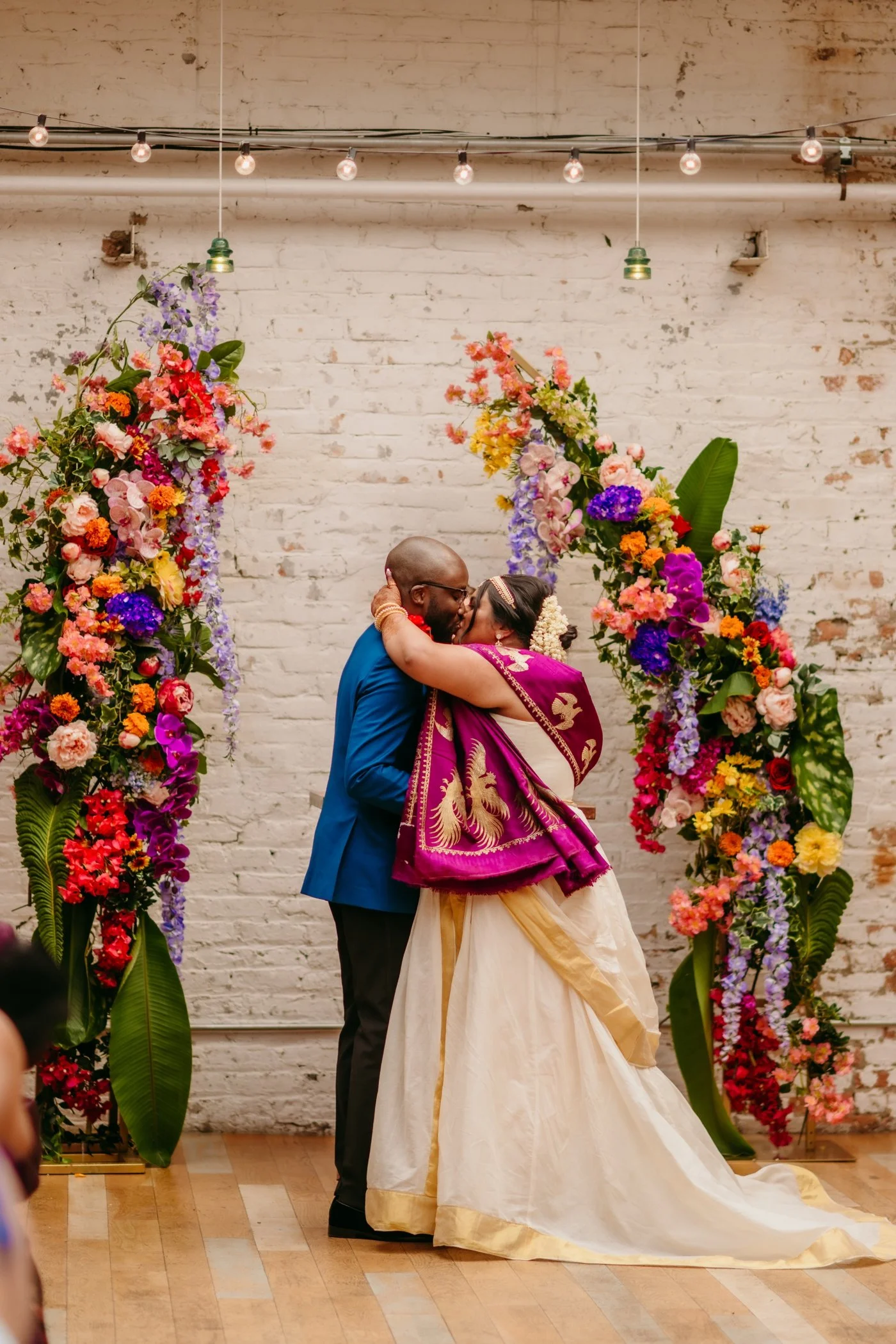 Bride and groom kissing in front of a colorful floral arch