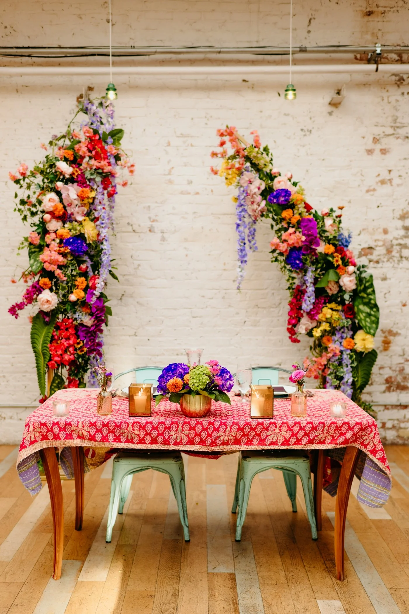 Sweetheart table with a red block print tablecloth in front of a colorful floral arch