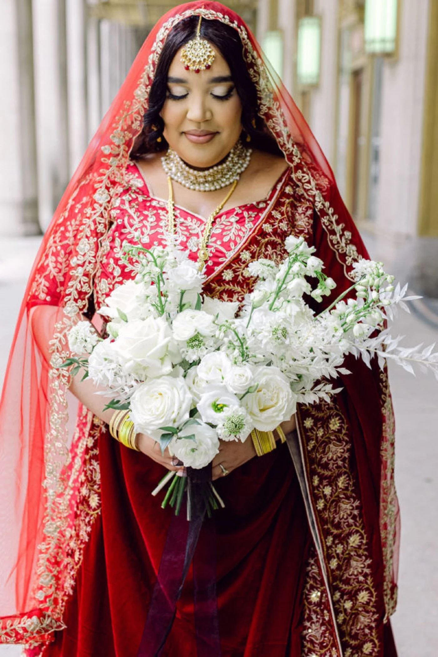 Bride wearing a red-and-gold saree and holding a bouquet of white flowers