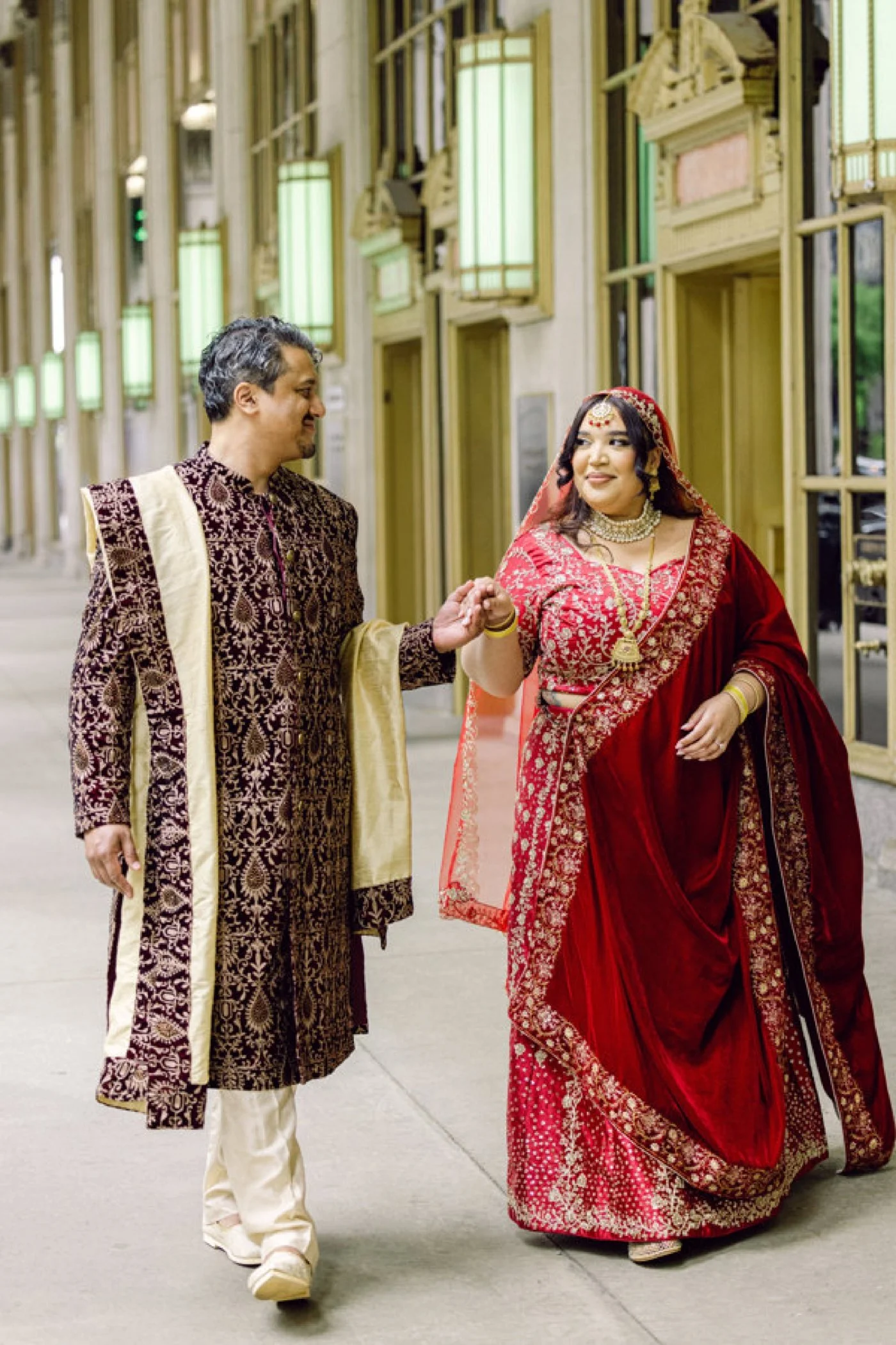 Bride and groom dressed in traditional Indian wedding attire and holding hands