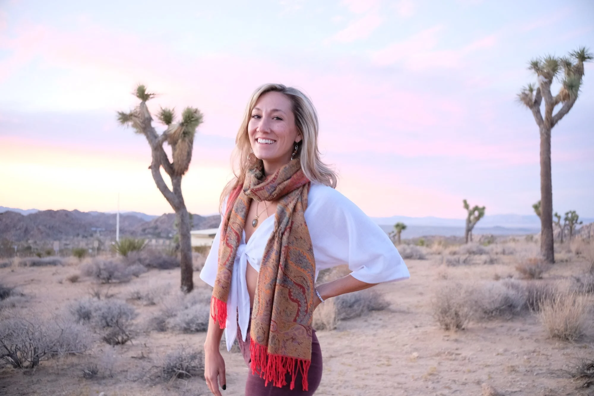 Astrologer Sarah Paasch smiling in the Joshua Tree desert at sunset, wearing a paisley scarf