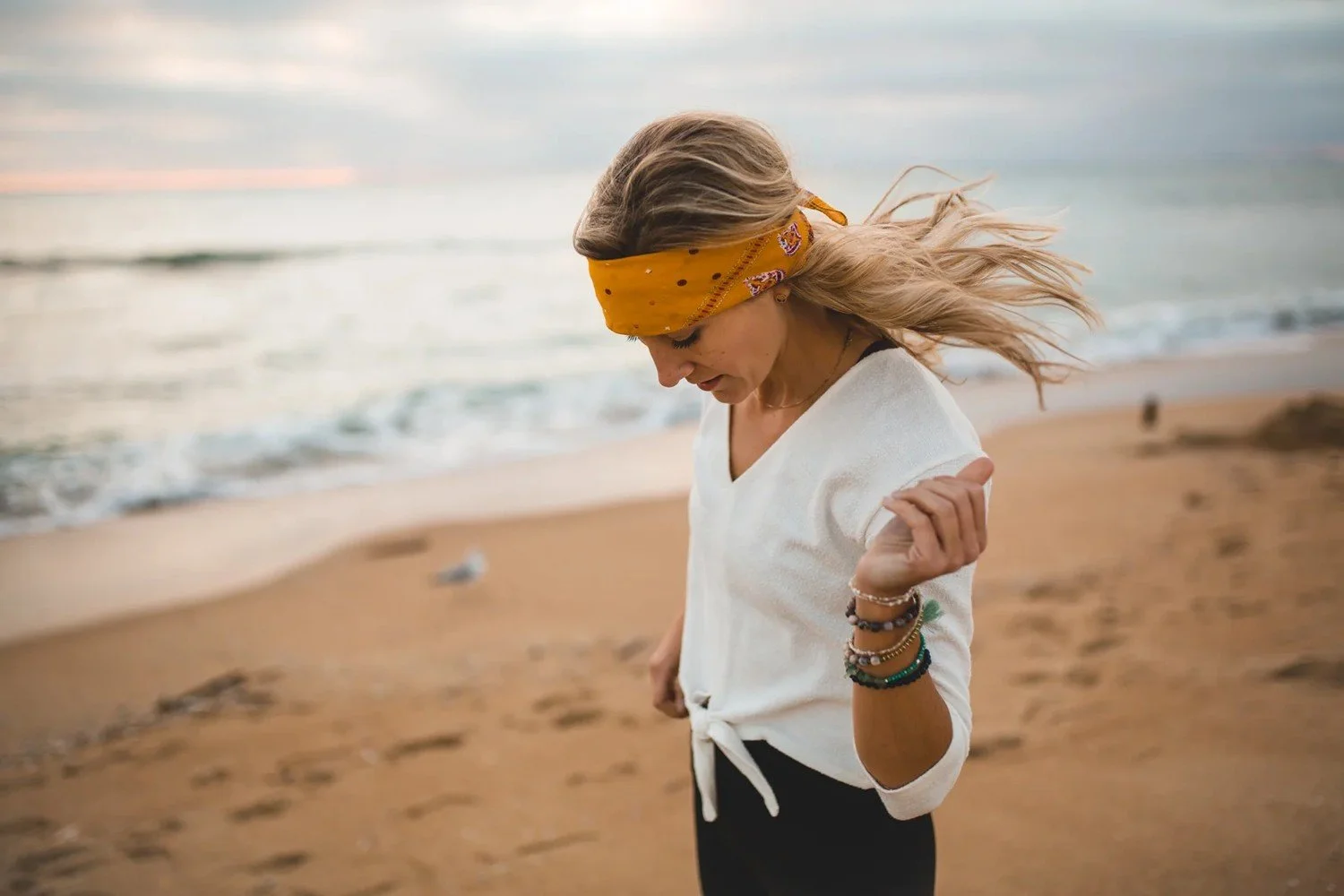 Astrologer Sarah Paasch in a yellow bandana walking barefoot on the beach at dusk