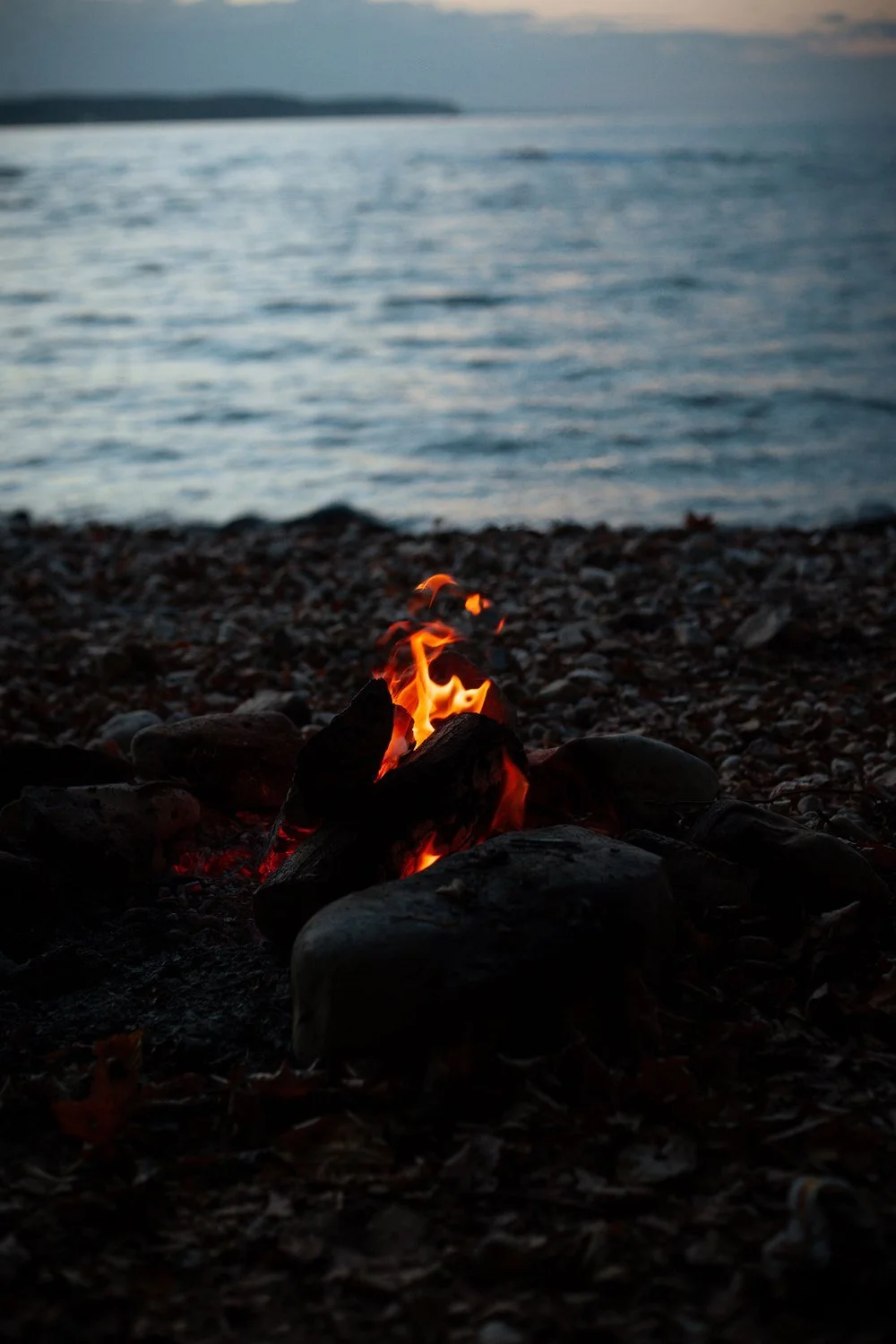 Small campfire on a pebble beach beside the water at dusk
