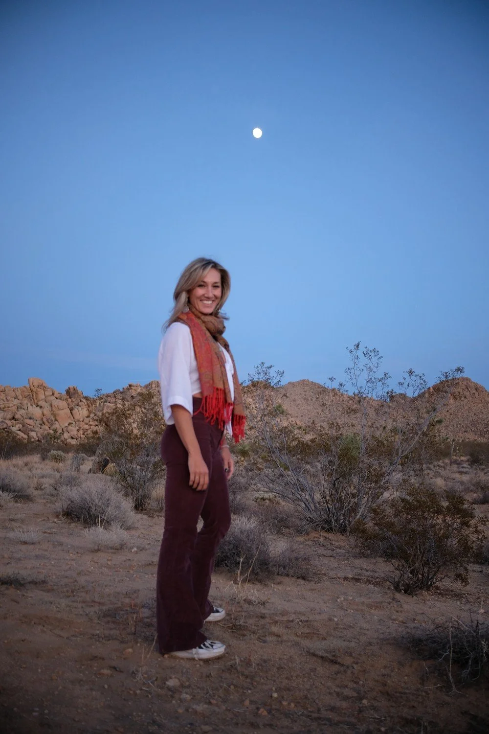 Astrologer Sarah Paasch standing in the desert at twilight with the full moon rising above