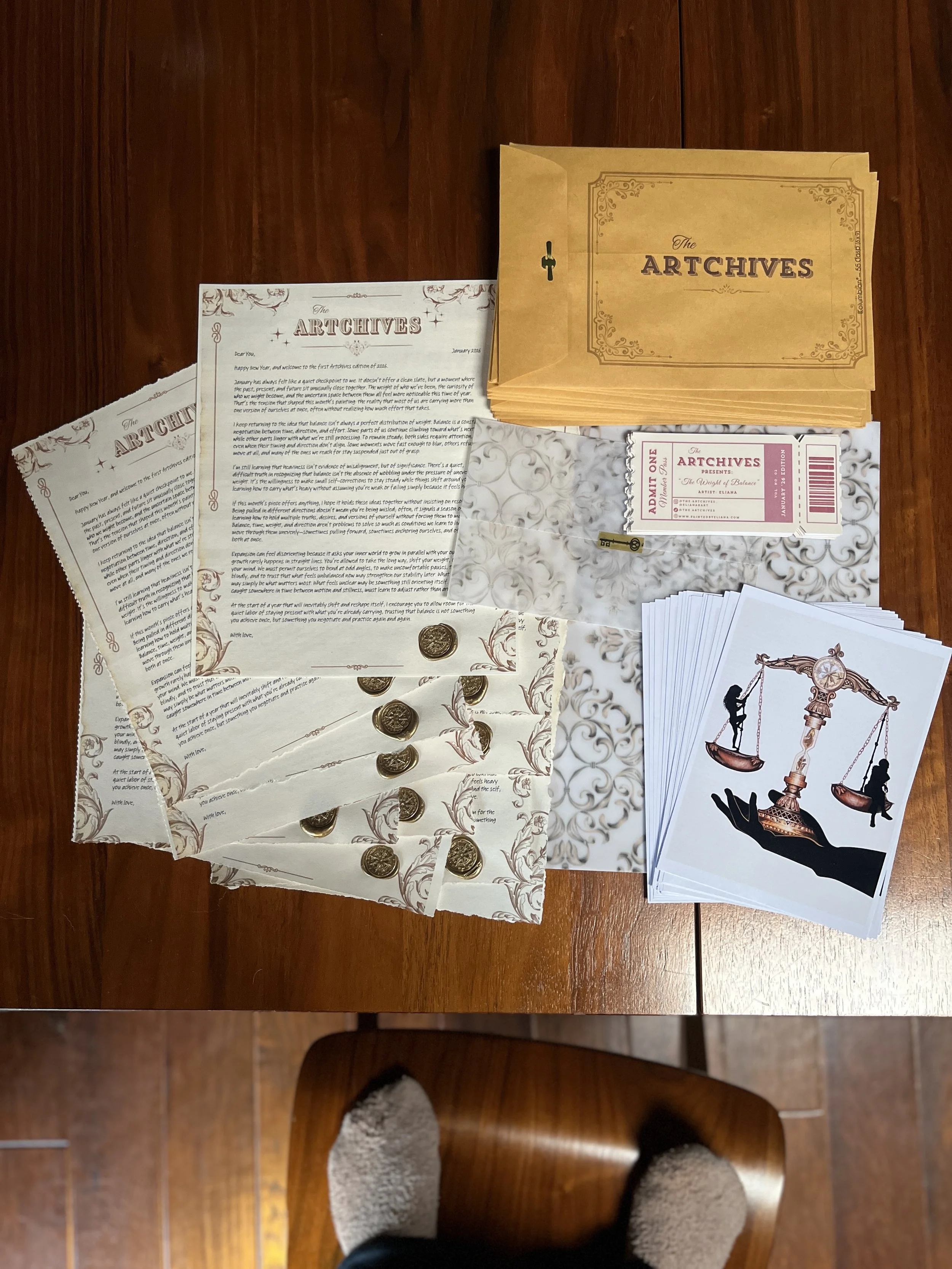 A wooden table with various papers, pamphlets, and cards related to the arts and an archive collection. There are seal stickers, a stack of brown folders, comic-style cards with a scale balancing illustration, and a paper with printed text.