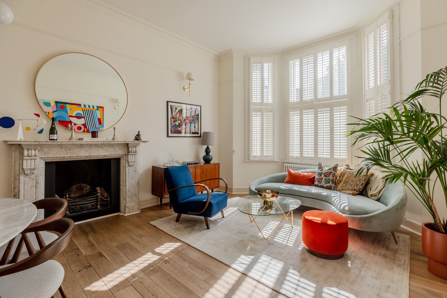 Living room with a marble fireplace, a bay window with white shutters and a curved grey sofa on a rug
