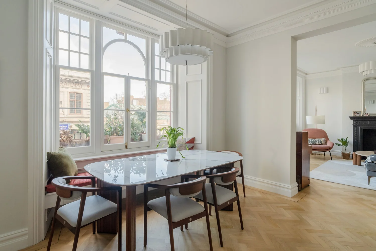 A bright dining room with a marble topped table and wooden chairs beside tall windows