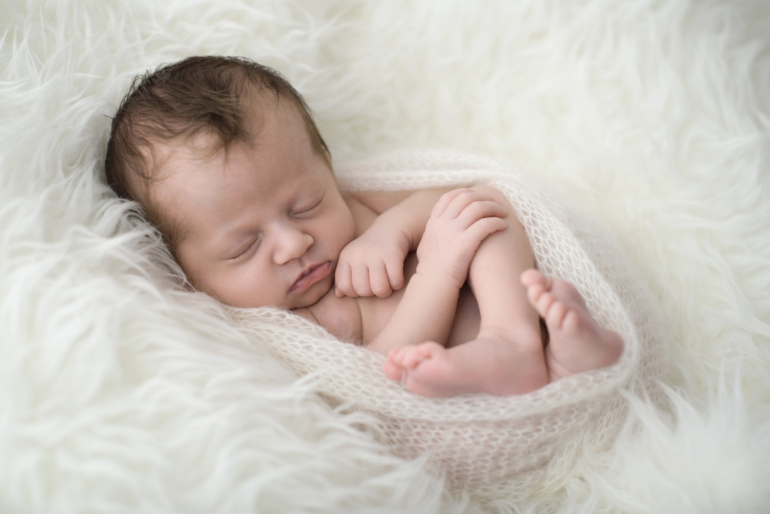 newborn curled up asleep in white furry wrap