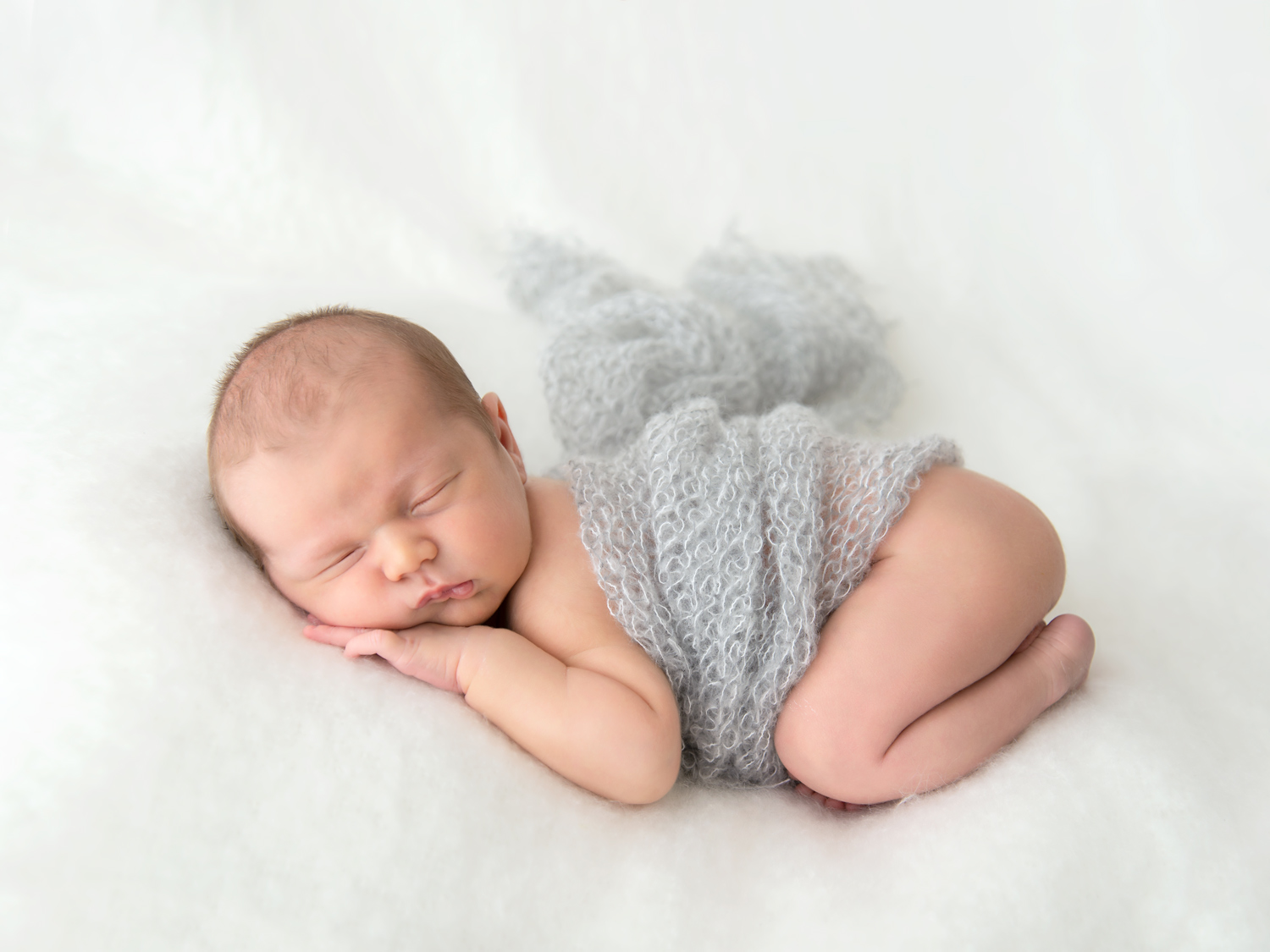 newborn sleeping on soft white blanket with grey knitted wrap