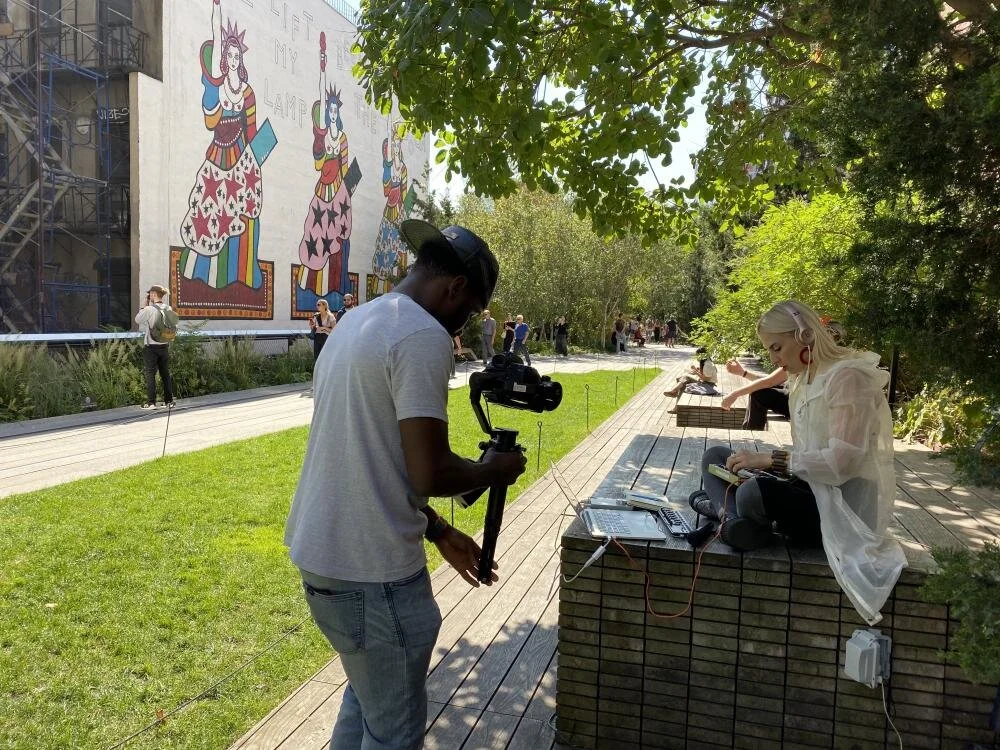 Alarke New York City Listening to Headphones Being Video Recorded Mural on Building in Background.jpg