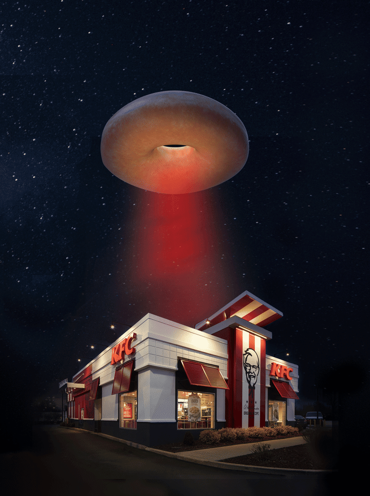 A glazed donut hovering like a flying saucer over a KFC at night, beaming down a red tractor beam