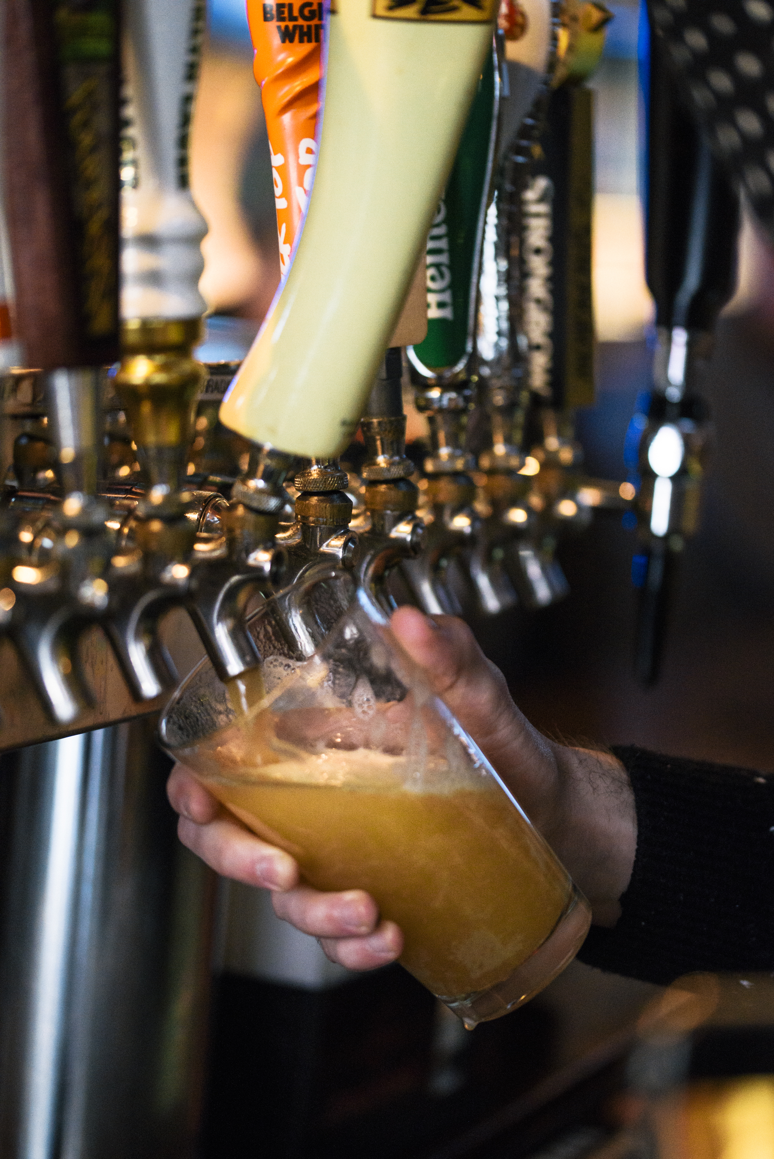 close up of bartender pouring a light draft beer into glass pint glass