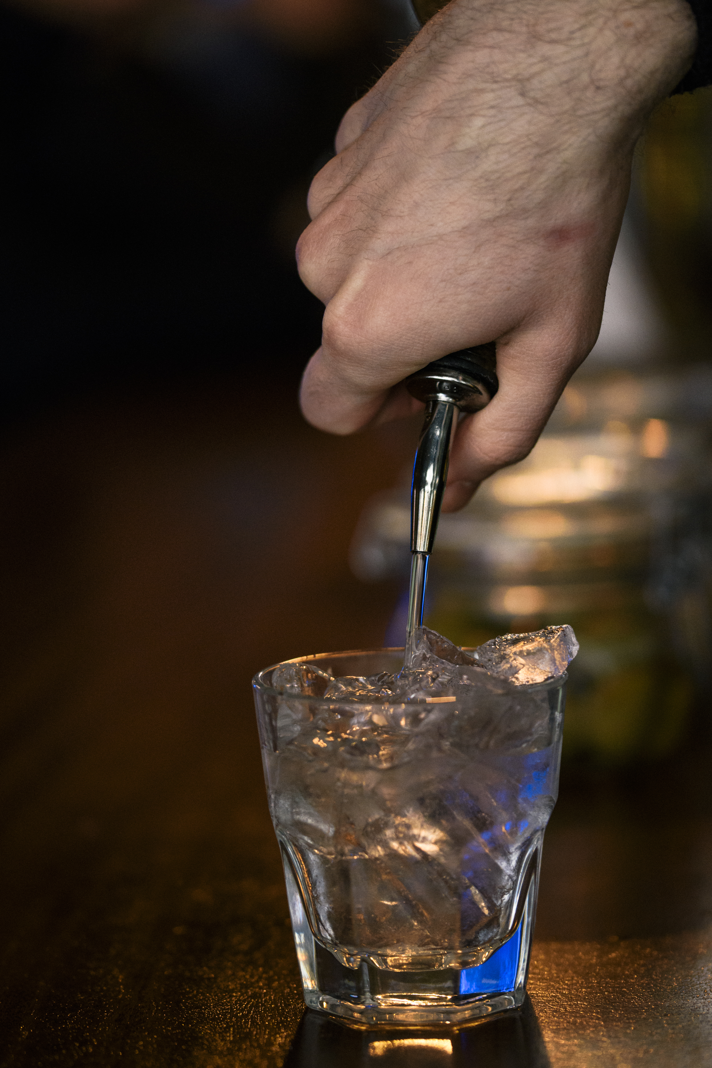 hand of bartender pouring vodka into short glass with ice