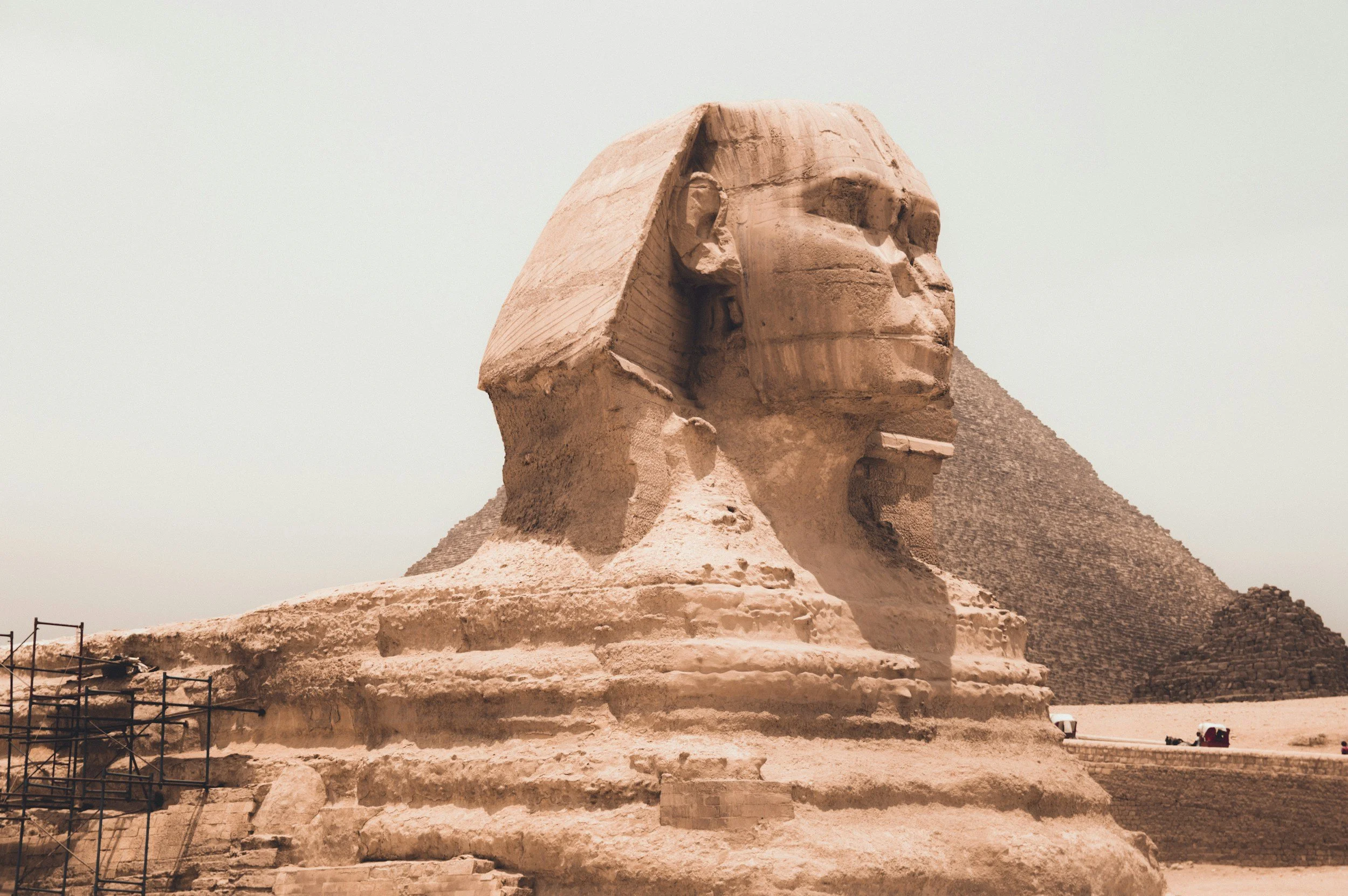 Close-up of the Great Sphinx of Giza with a pyramid in the background, under a clear sky.