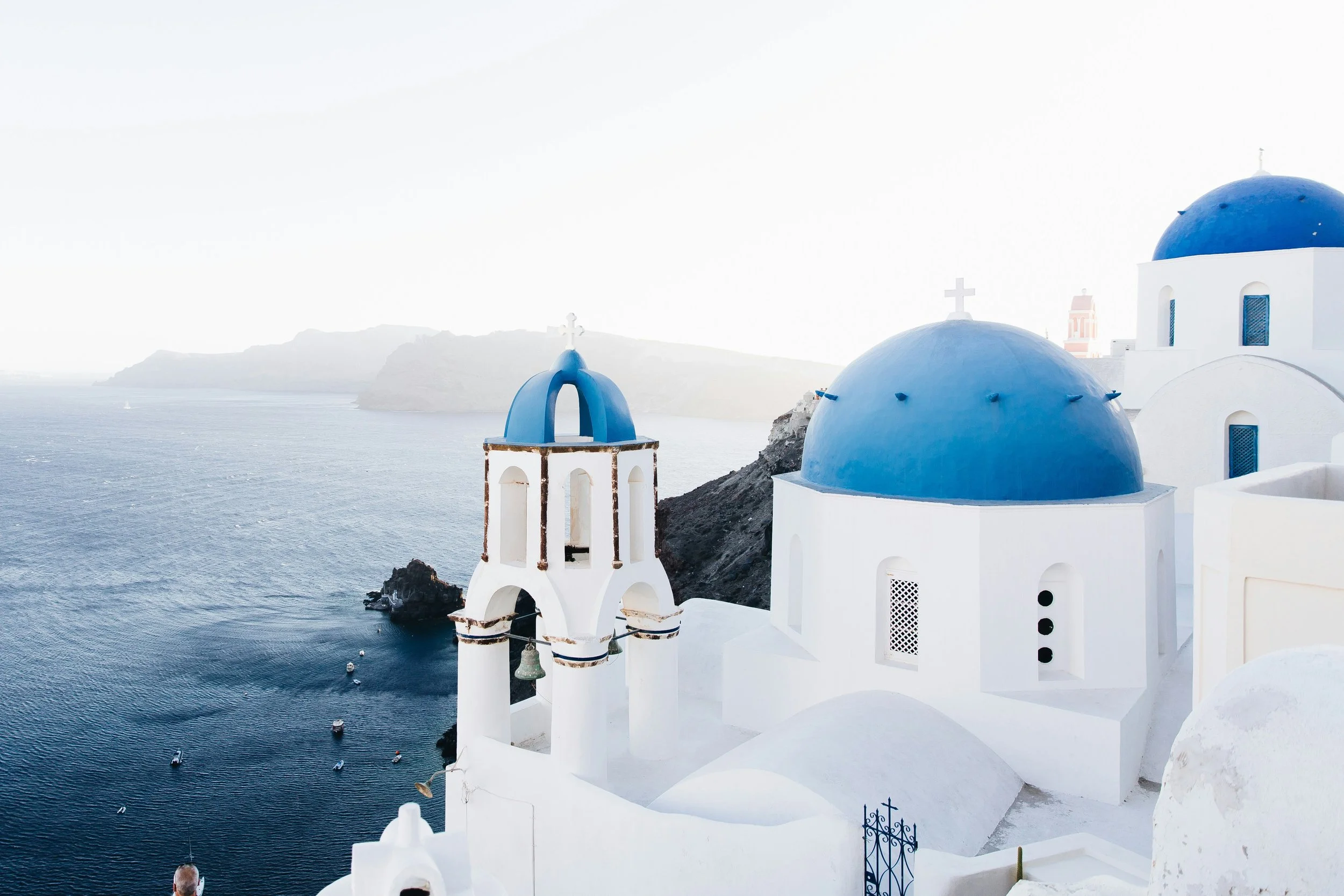 White church with blue domes and crosses overlooking the sea in Santorini, Greece.