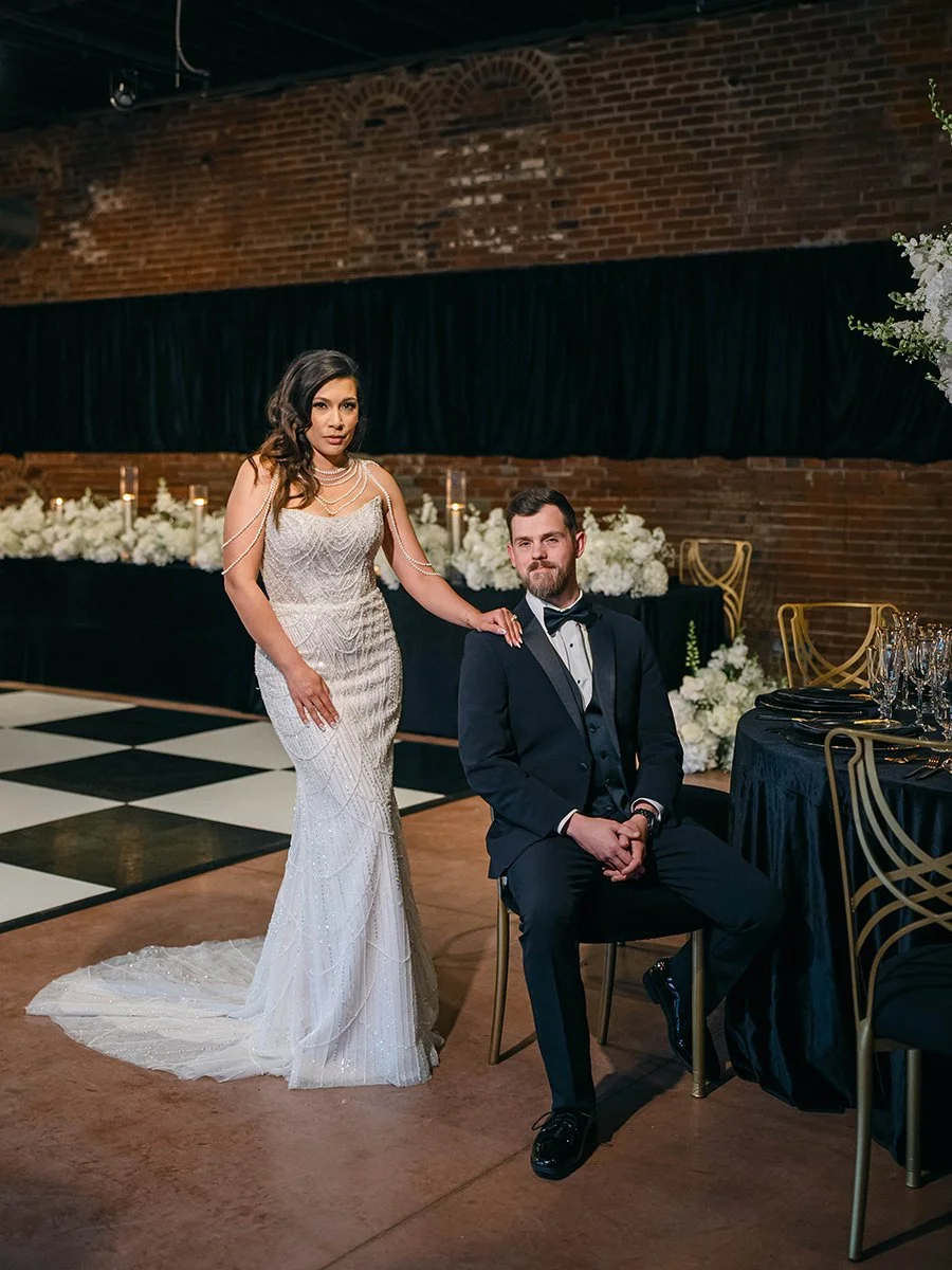 Bride and groom sitting at a table covered in white wedding flowers at the Gatsby Event Venue in St. Louis.
