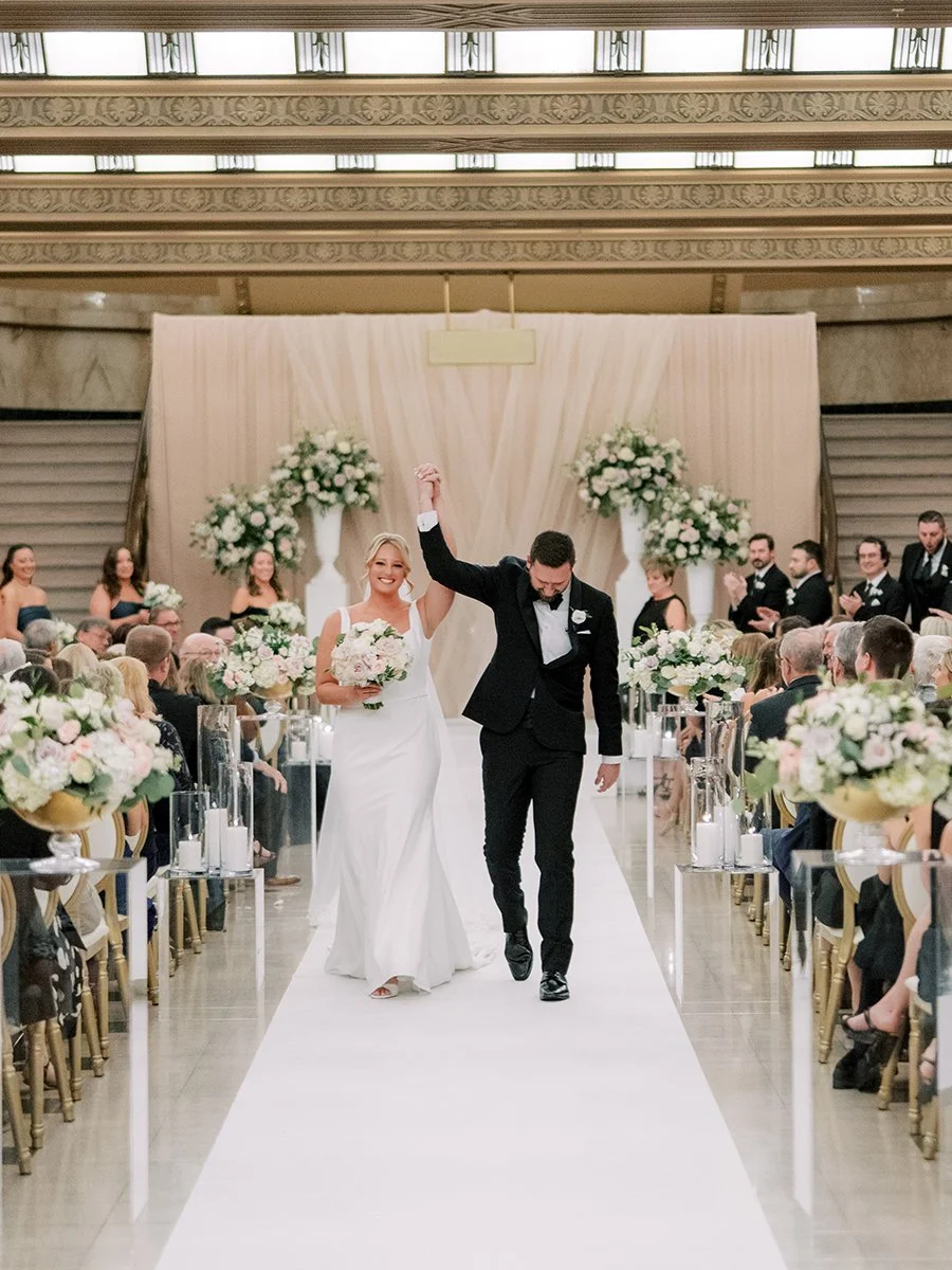 Bride and groom walking up ceremony aisle with blush and white flowers for a wedding at the Stifel Theater in St. Louis.