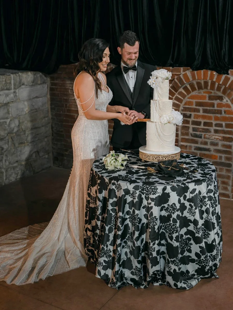 Bride and groom cutting a white multi-tiered wedding cake at the Gatsby Events Venue in St. Louis.