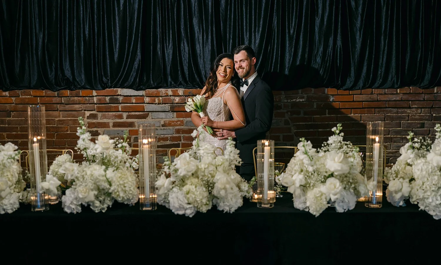 Bride and groom at their head table covered in white wedding flowers at the Gatsby Events Venue in St. Louis.