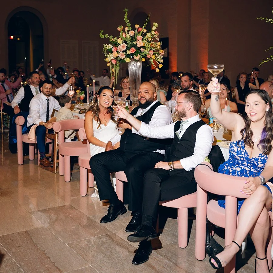 Bride and groom sitting at their head table enjoying wedding day toasts at the St. Louis Art Museum with flowers designed by Belli Fiori.