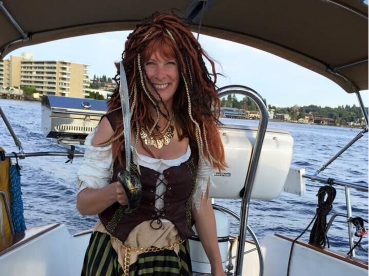 Jen Sarthou is wearing a pirate costume and standing on a sailboat