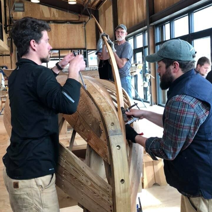Josh Anderson helps plank a wooden boat with two volunteers