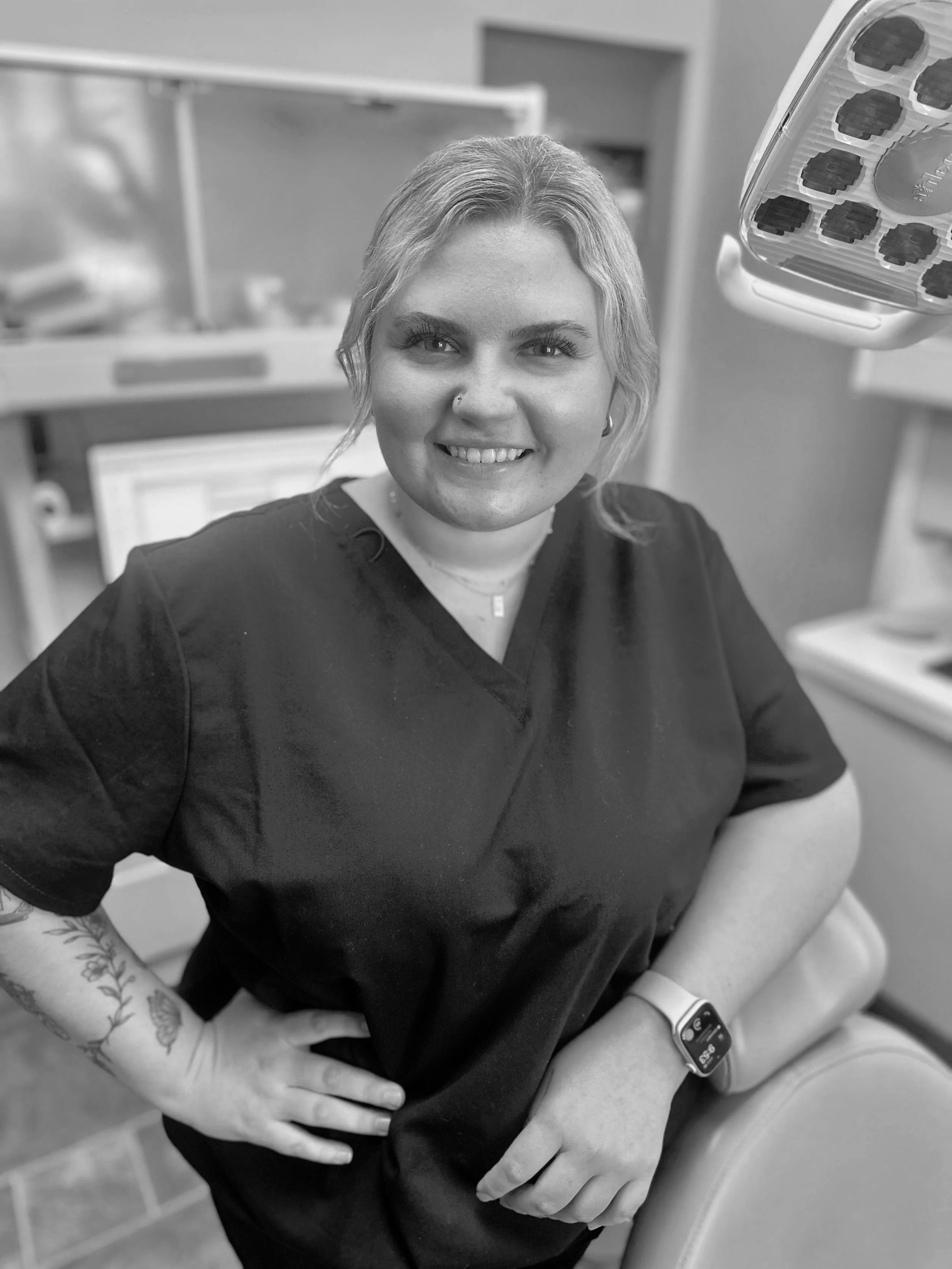 A smiling woman in medical scrubs taking a blood sample in a clinical setting.