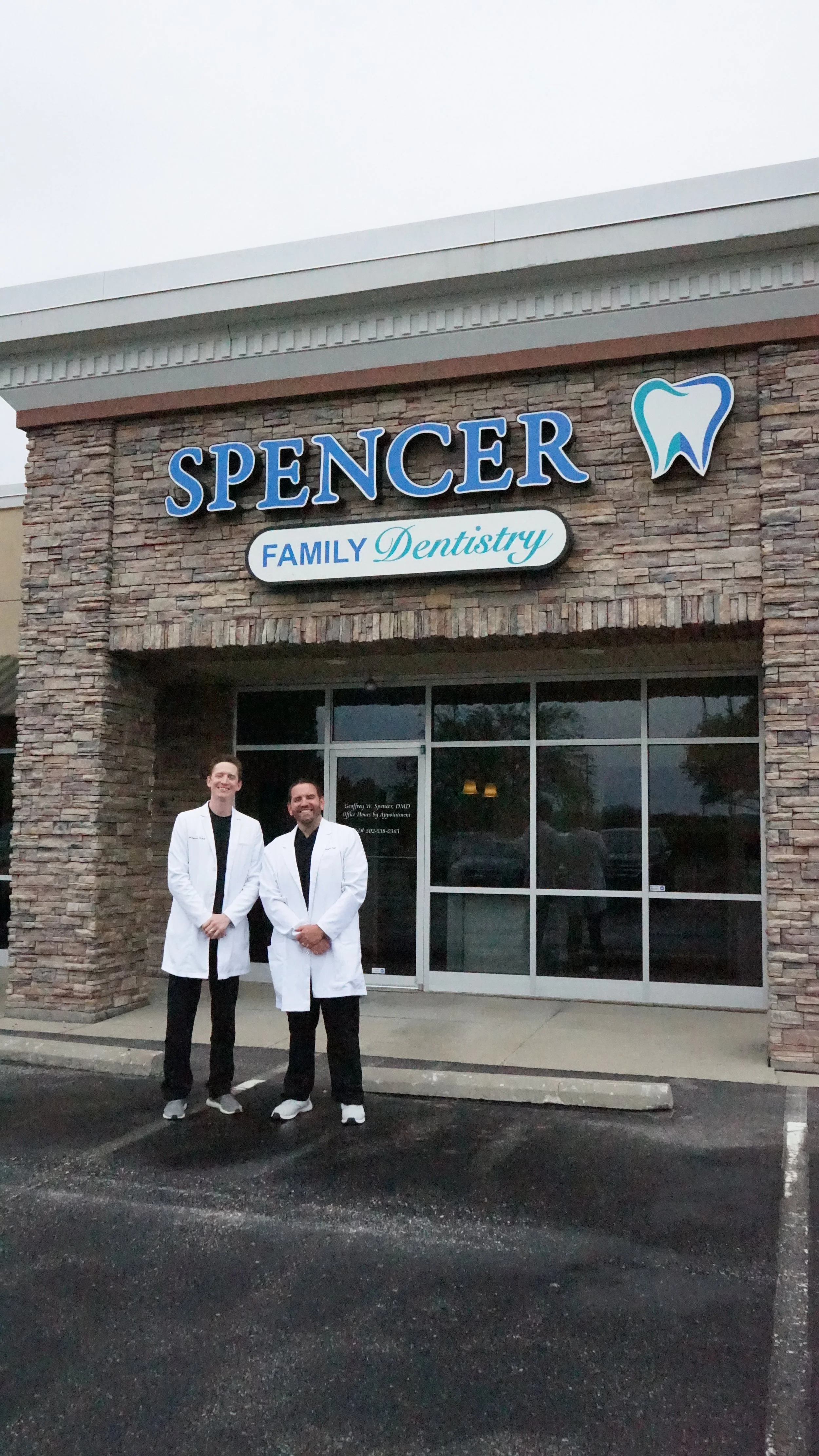 Two dentists standing outside of a dental office with a sign that reads 'Spencer Family Dentistry' and a tooth logo.
