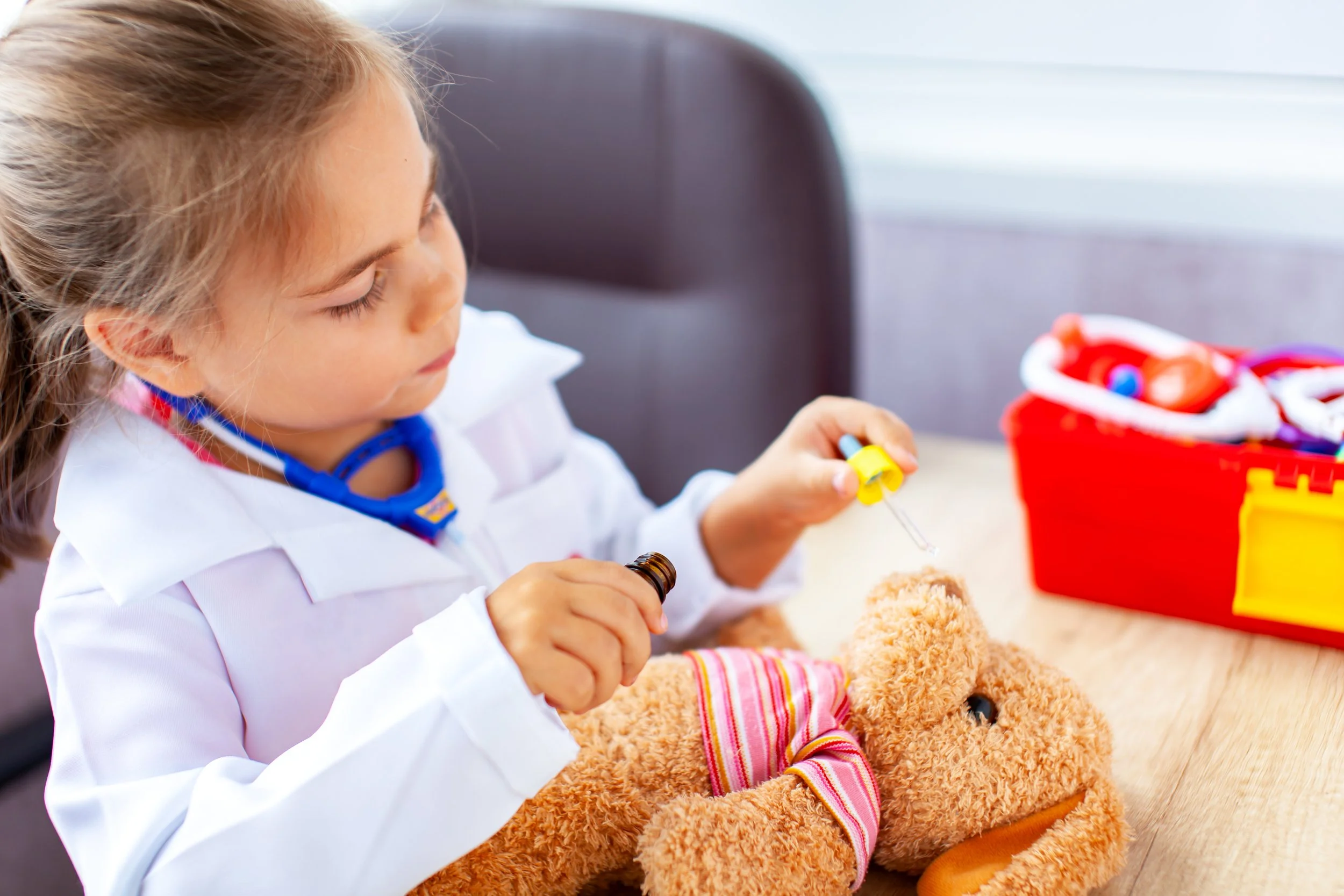 Young girl wearing doctor costume and playing doctor on a stuffed toy