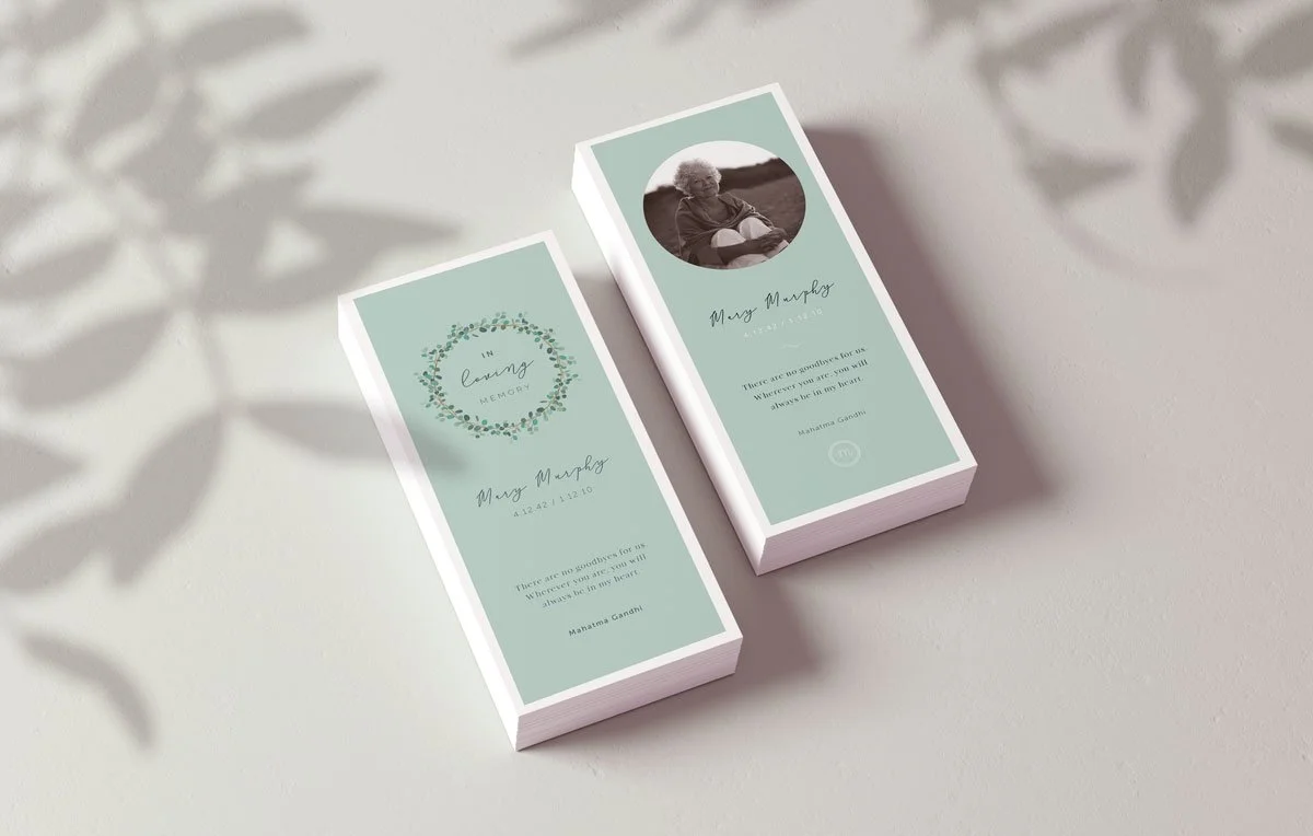 Two funeral program booklets with a light green cover, one open and one closed, featuring a black and white photo of an elderly woman, floral design, and a quote by Mahatma Gandhi.