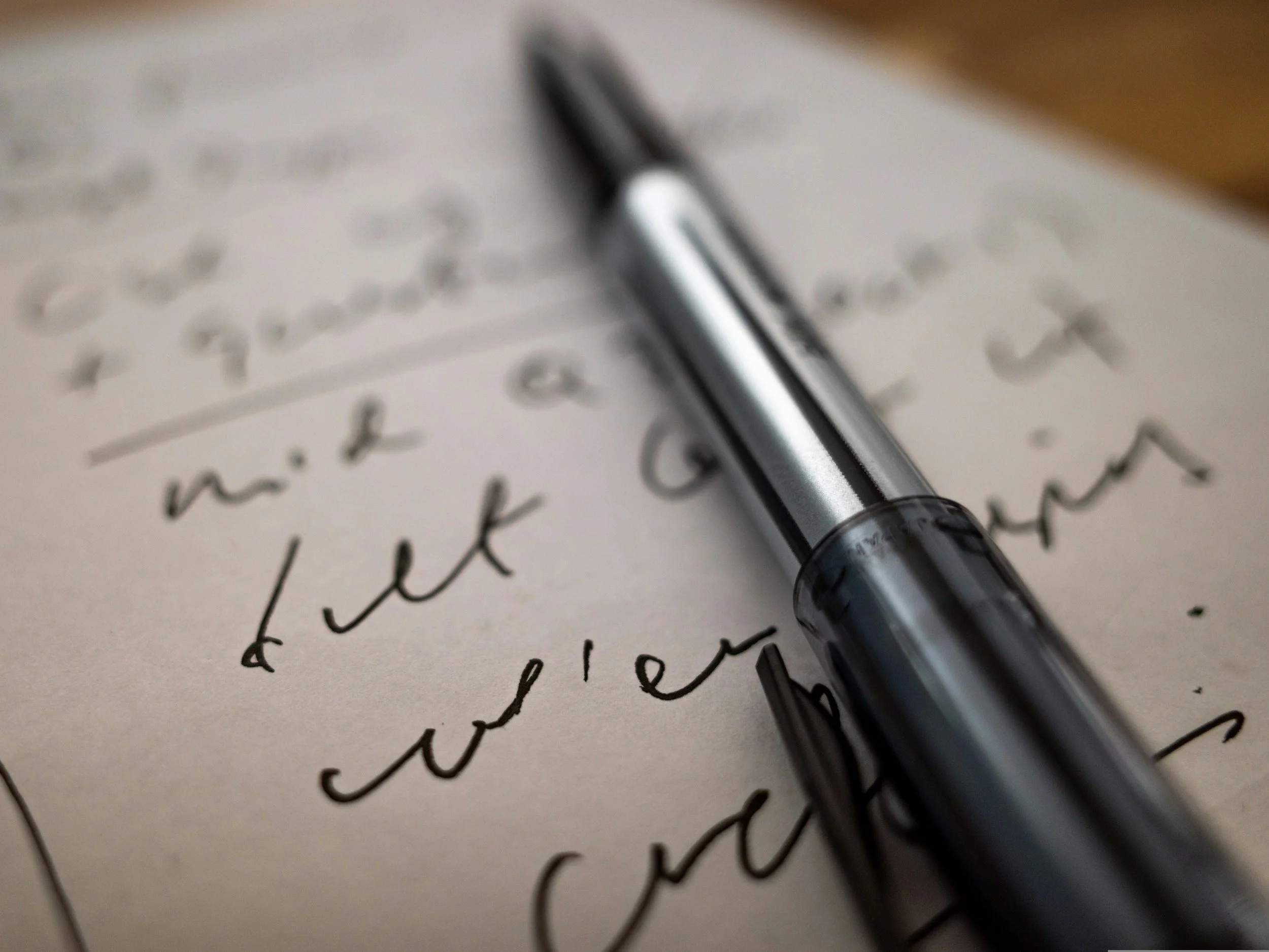 Close-up of a silver and black gel pen resting on handwritten notes on white paper.